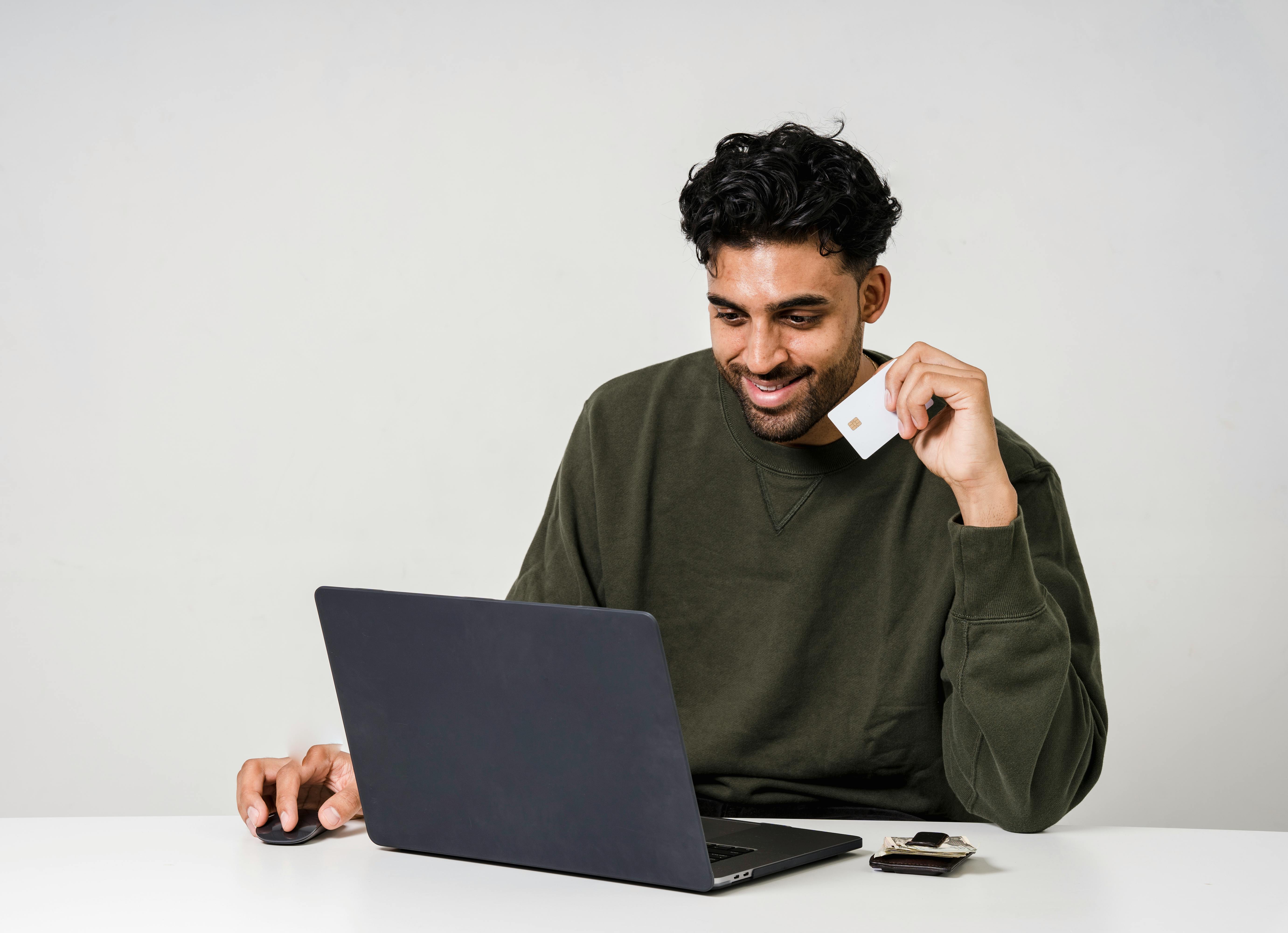 A man looks at his laptop and smiles while holding a credit card 